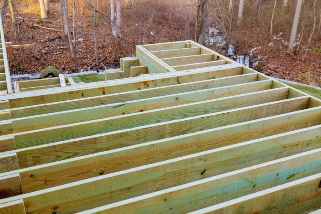 New wooden building foundation framework under construction in a wooded area.